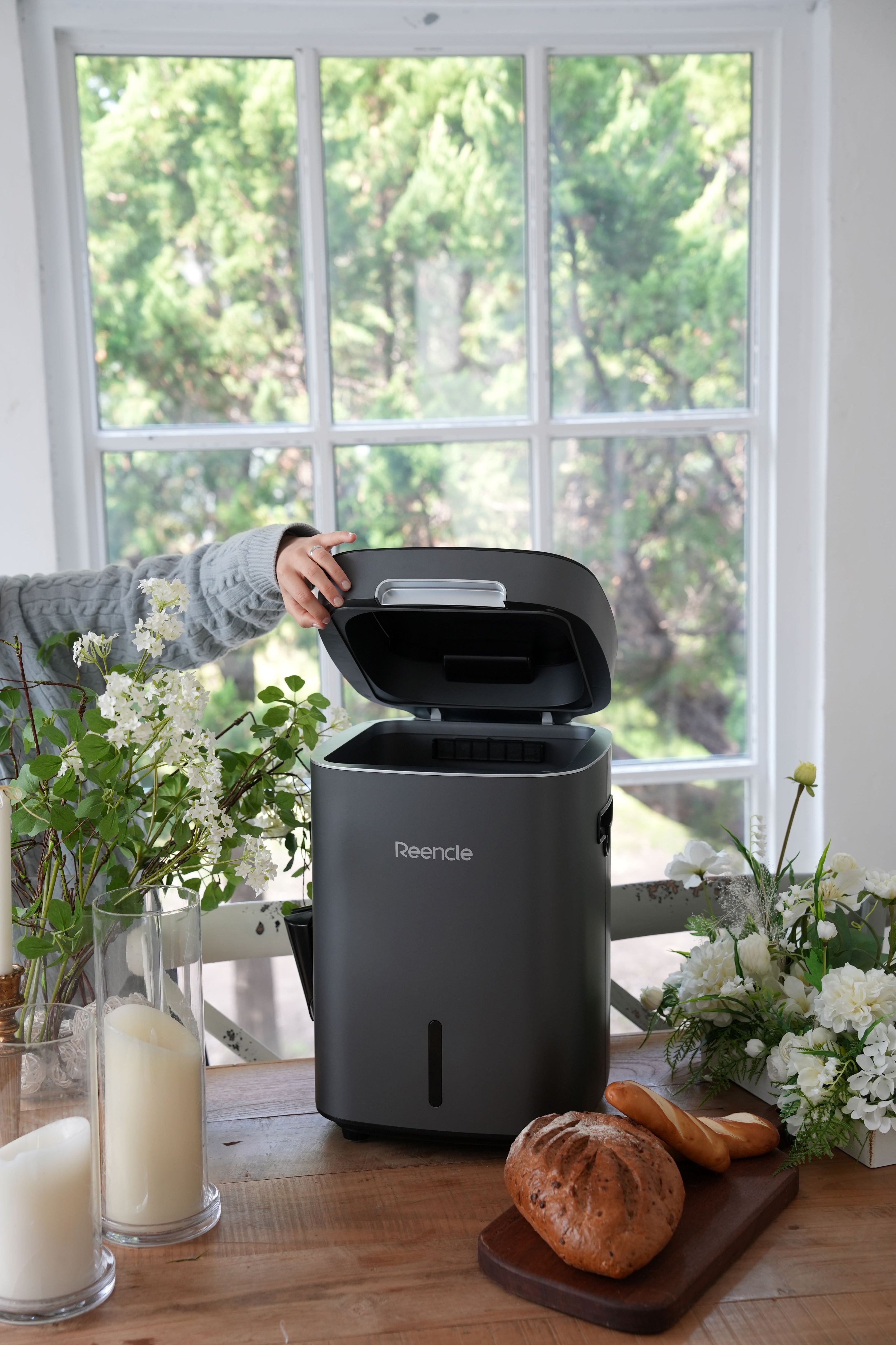 Photo of a grey Reencle Prime Composter on a wooden table beside bread and candles
